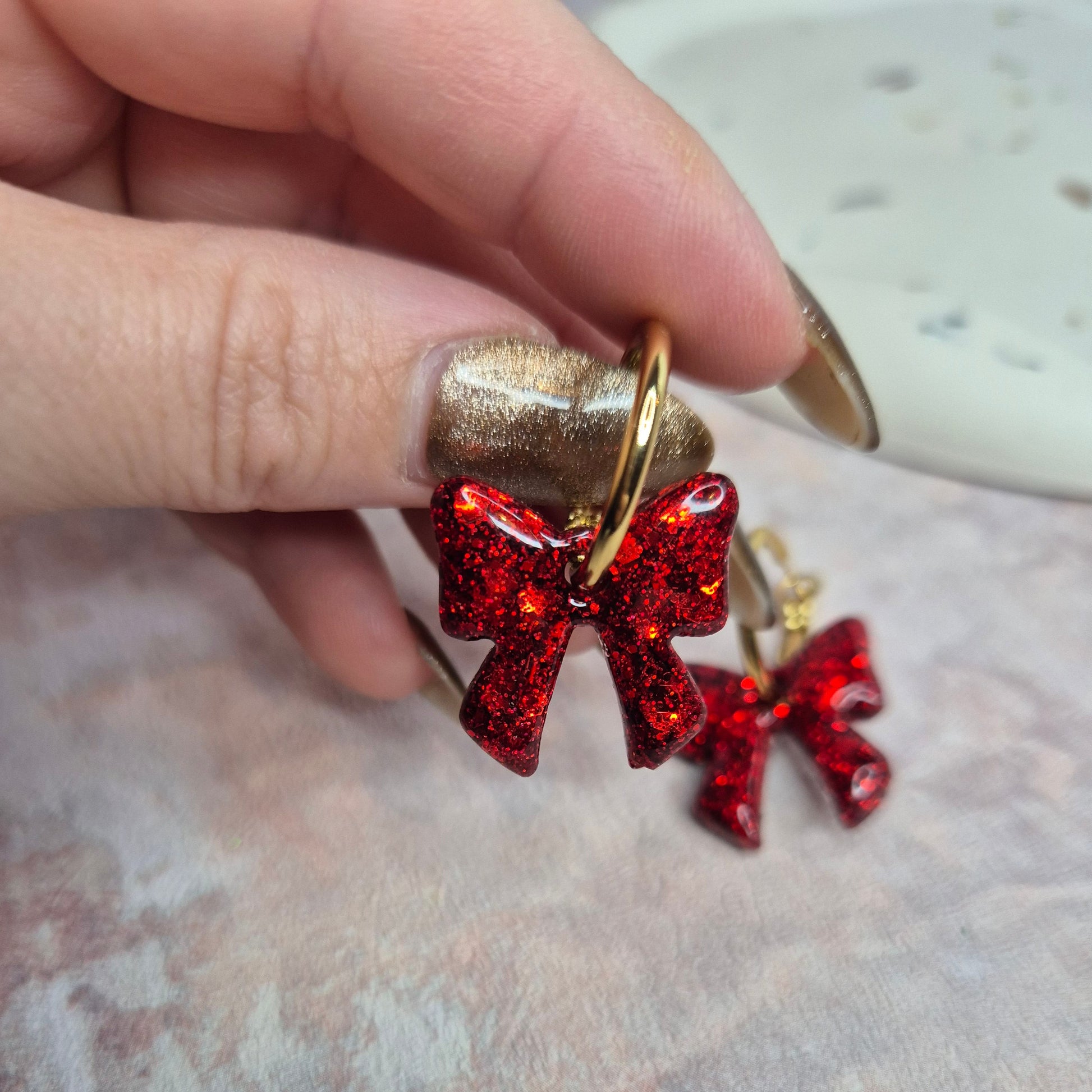 Red bow-shaped earrings held by a hand against a textured surface
