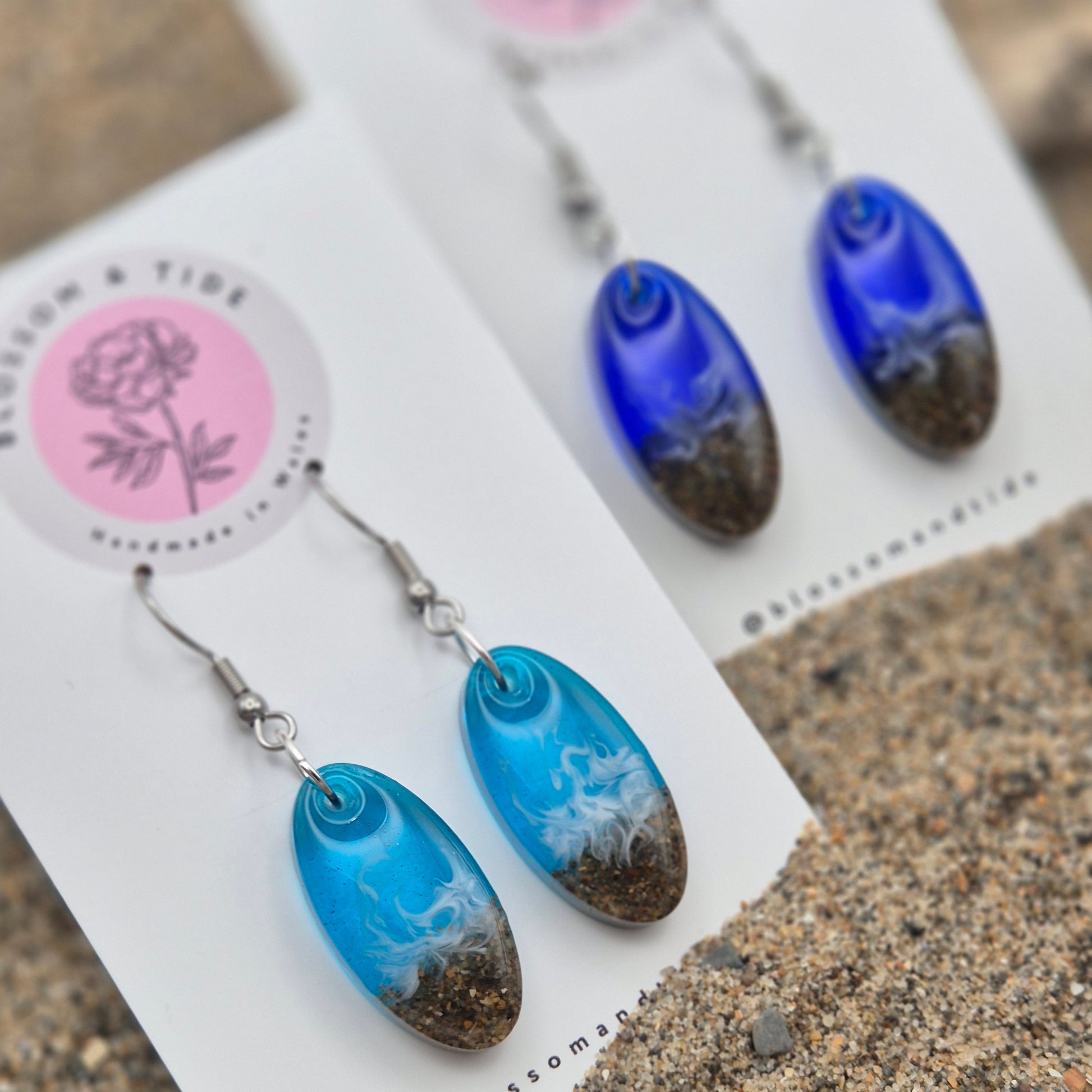 Handmade blue oval drop earrings. Made with real sand from Welsh beaches. Replicating the look of sea and sand. Displayed on a blossom and tide branded earring card.