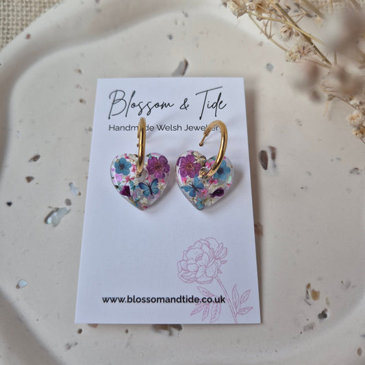 Floral earrings on a card with 'Blossom & Tide' branding, placed on a textured surface.