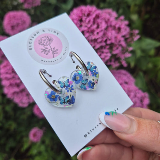 handmade resin earrings, heart shaped with real pressed forget-me-not flowers and blue butterflies. On stainless steel hoops.