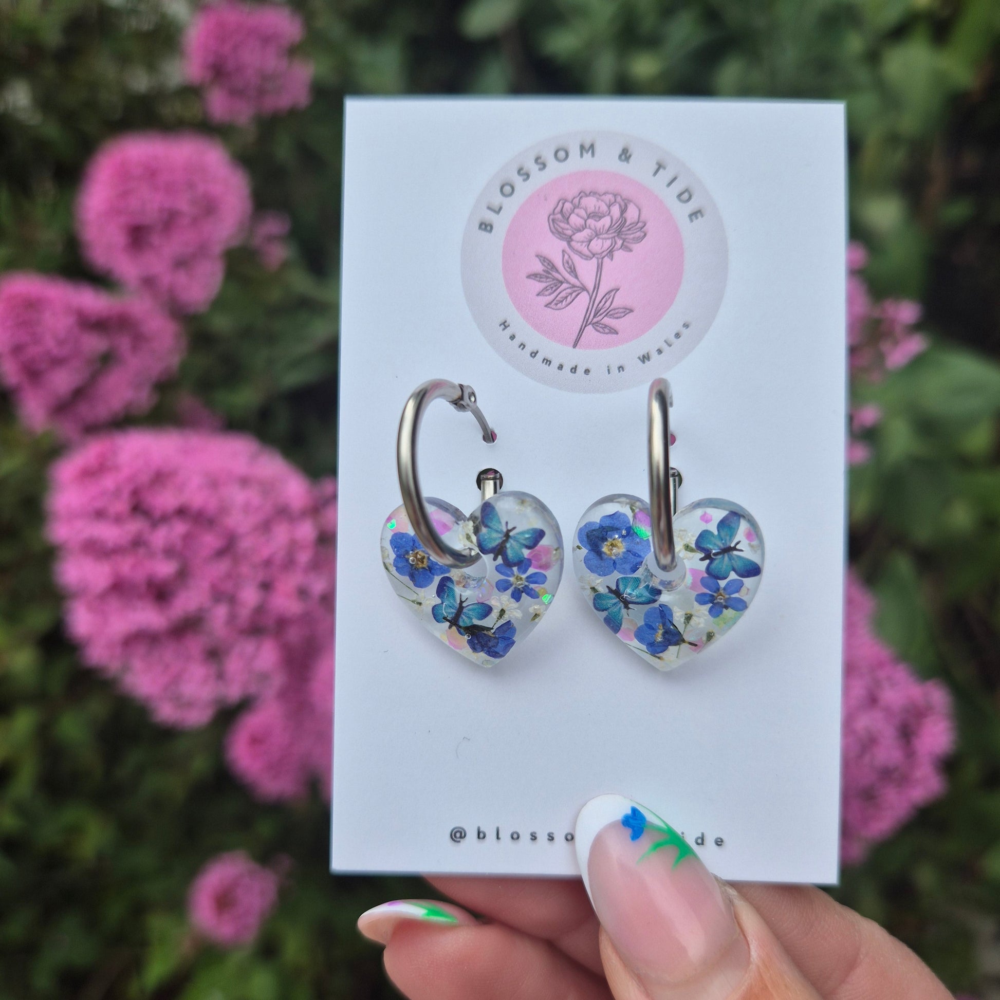 handmade resin earrings, heart shaped with real pressed forget-me-not flowers and blue butterflies. On stainless steel hoops.