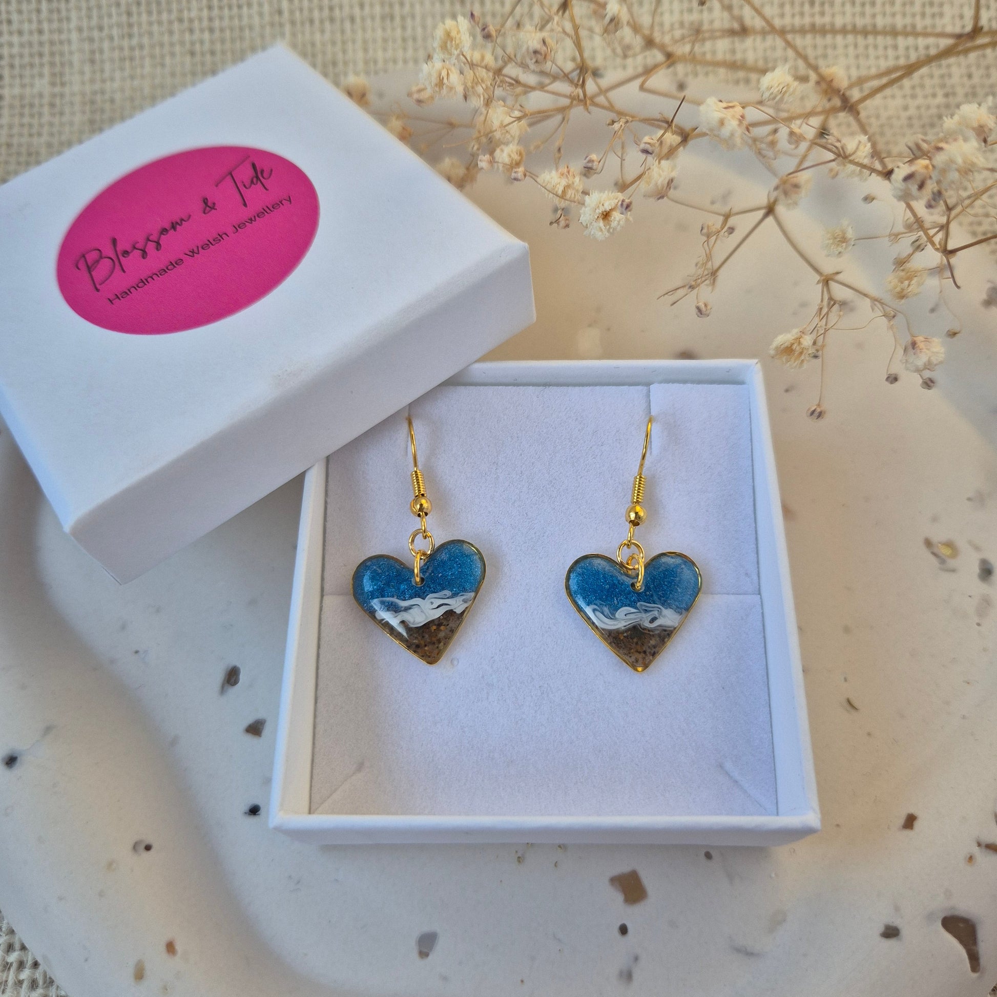Heart-shaped earrings in a box with a pink label on a textured surface