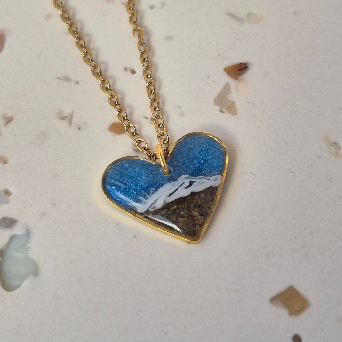 Sand necklace with a blue and gold pendant on a textured surface