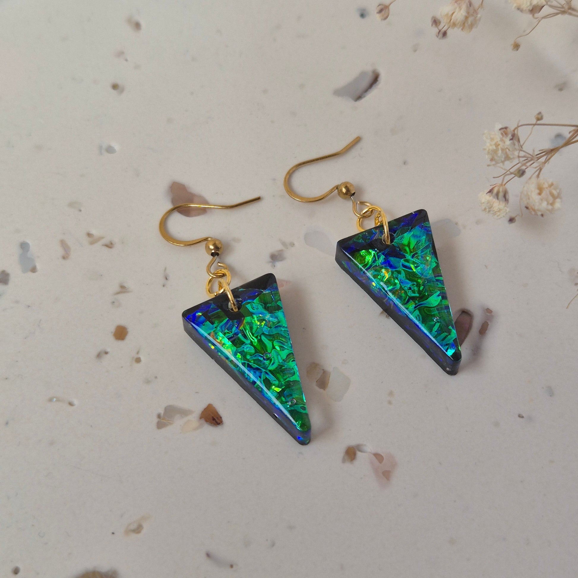 Triangular earrings with green and black iridescent finish on a light background