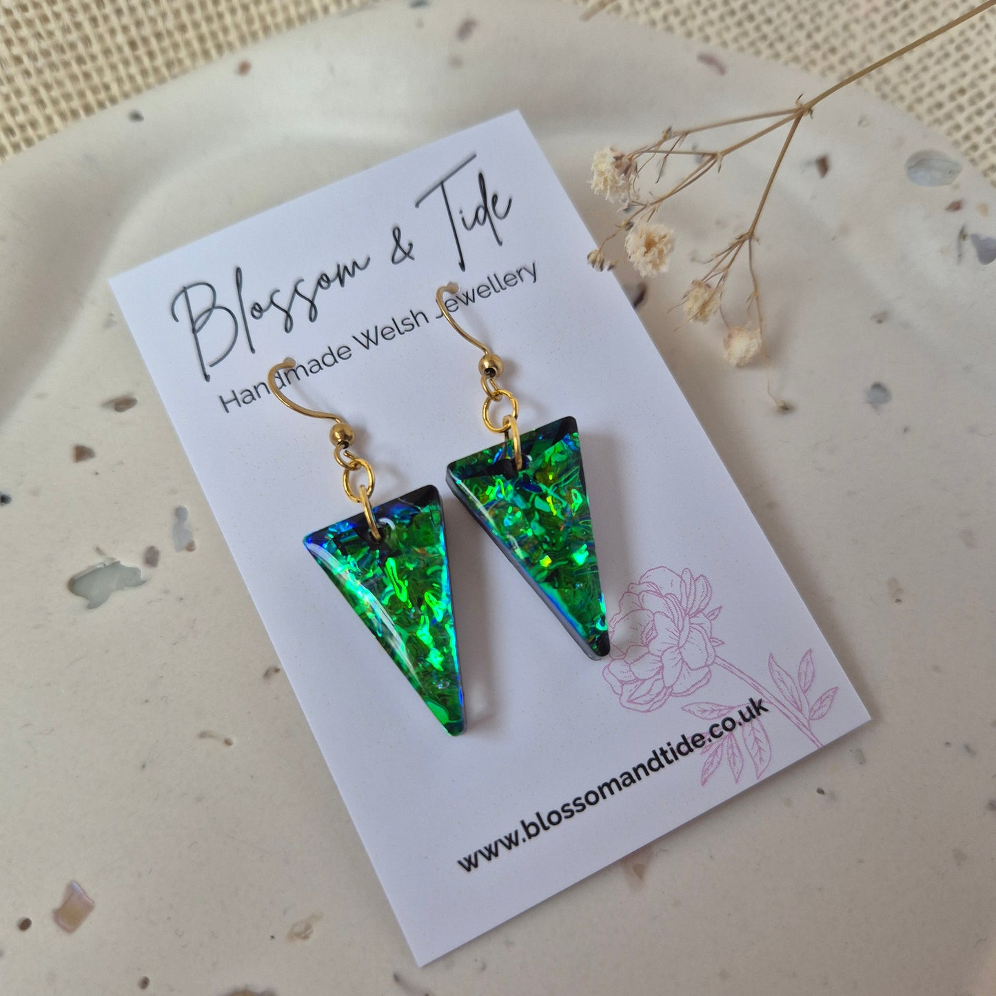 Green triangle-shaped earrings on a card with floral design