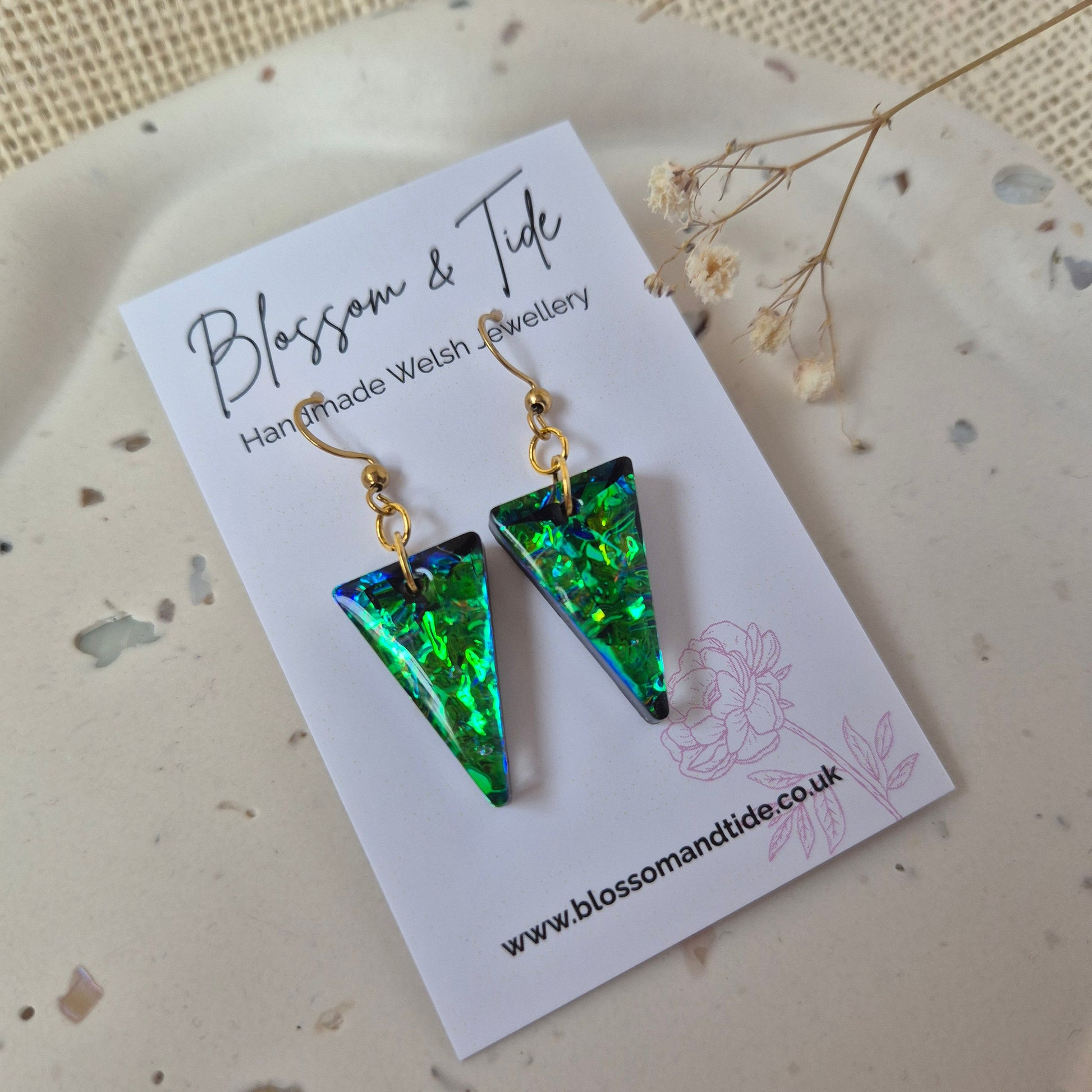 Green triangle-shaped earrings on a card with floral design