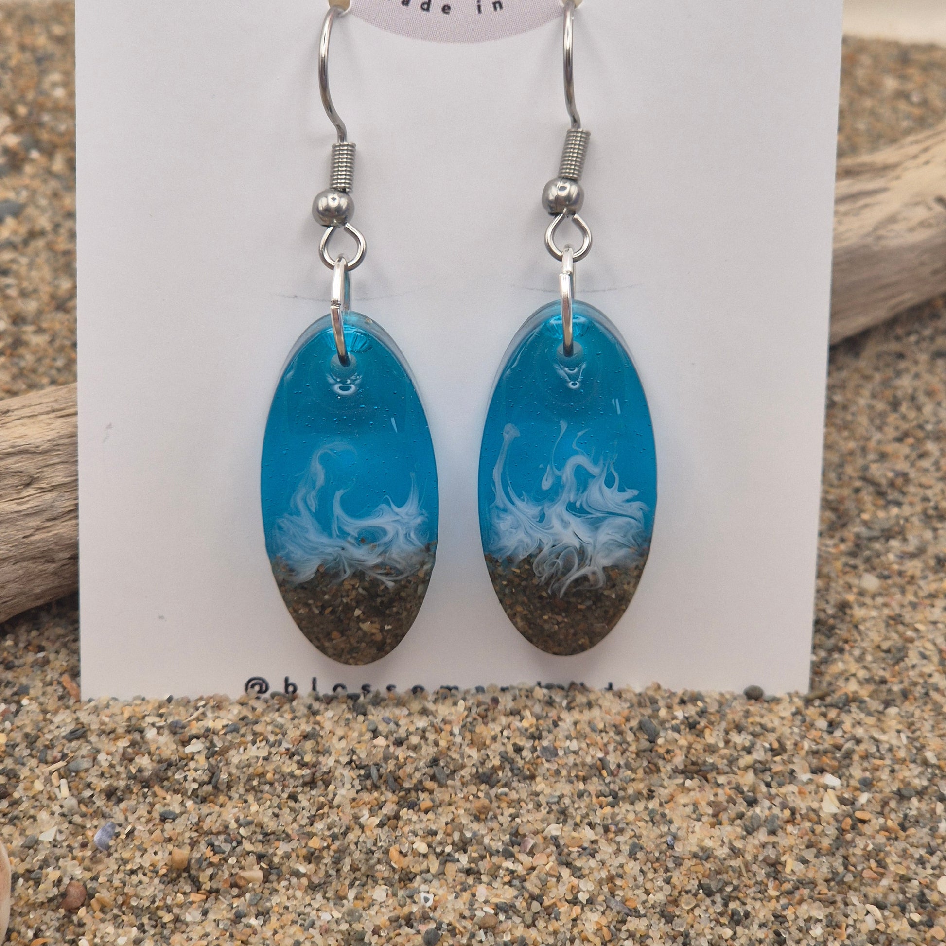 Handmade blue oval drop earrings. Made with real sand from Welsh beaches. Replicating the look of sea and sand. Displayed on a blossom and tide branded earring card.