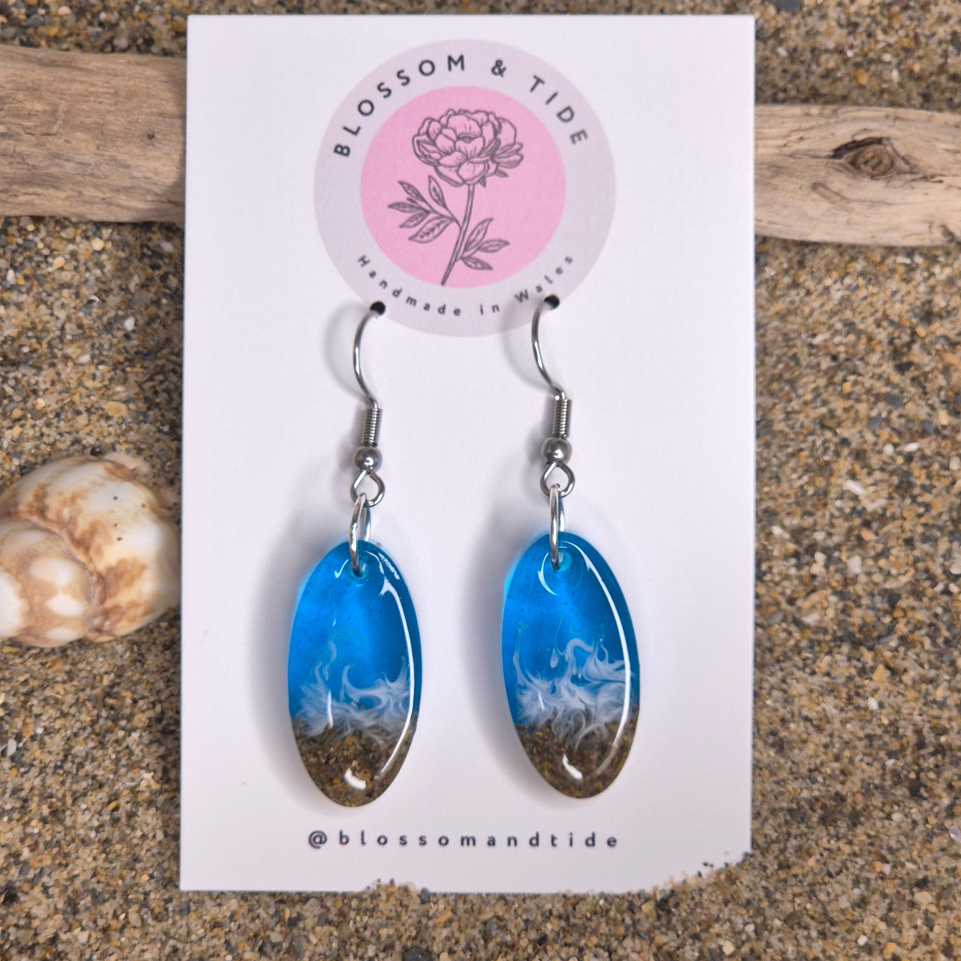 Handmade blue oval drop earrings. Made with real sand from Welsh beaches. Replicating the look of sea and sand. Displayed on a blossom and tide branded earring card.