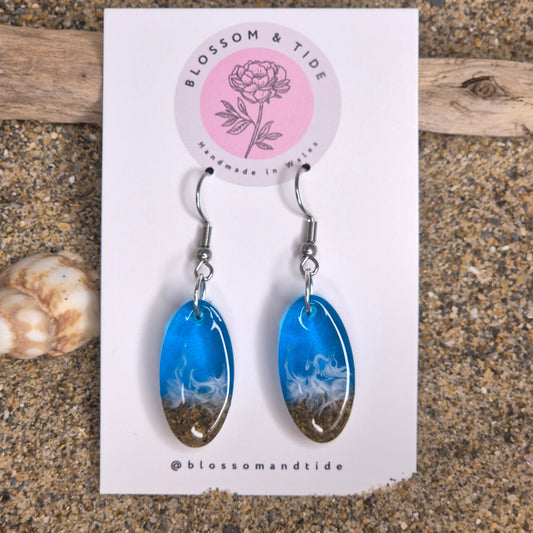 Handmade blue oval drop earrings. Made with real sand from Welsh beaches. Replicating the look of sea and sand. Displayed on a blossom and tide branded earring card.