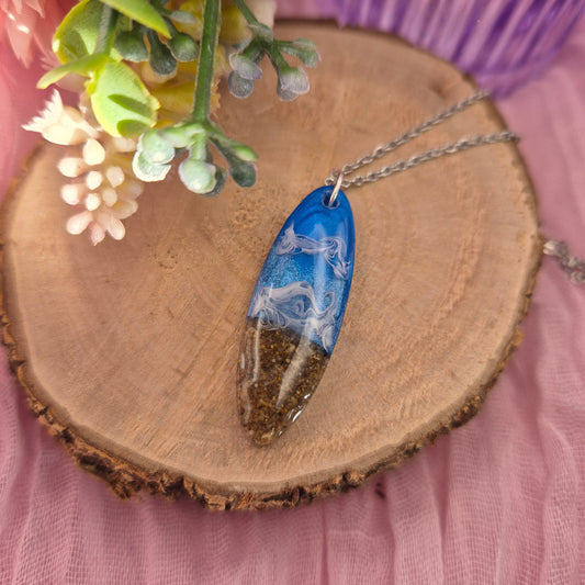 Handmade oval pendant necklace with real sand from Tenby beach, blue sea detail, and white wave ripples on a stainless steel chain.