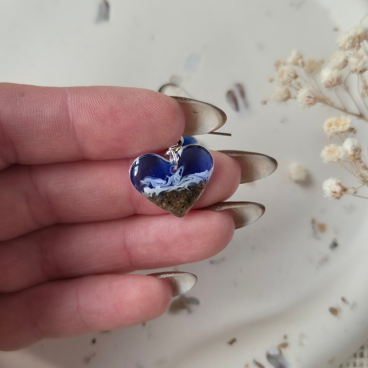 heart beach sand earring held by hand against a neutral background