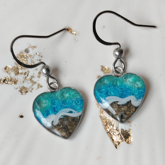 Heart-shaped earrings with blue and white ocean design with real welsh sand real we on a light background