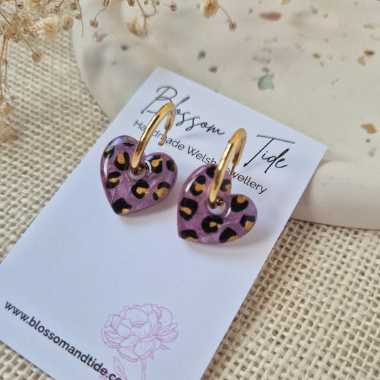 Pair of purple heart-shaped earrings with gold leopard print accents on a branded card.
