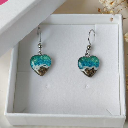 Heart-shaped earrings with blue and white ocean design with real welsh sand real we on a light background
