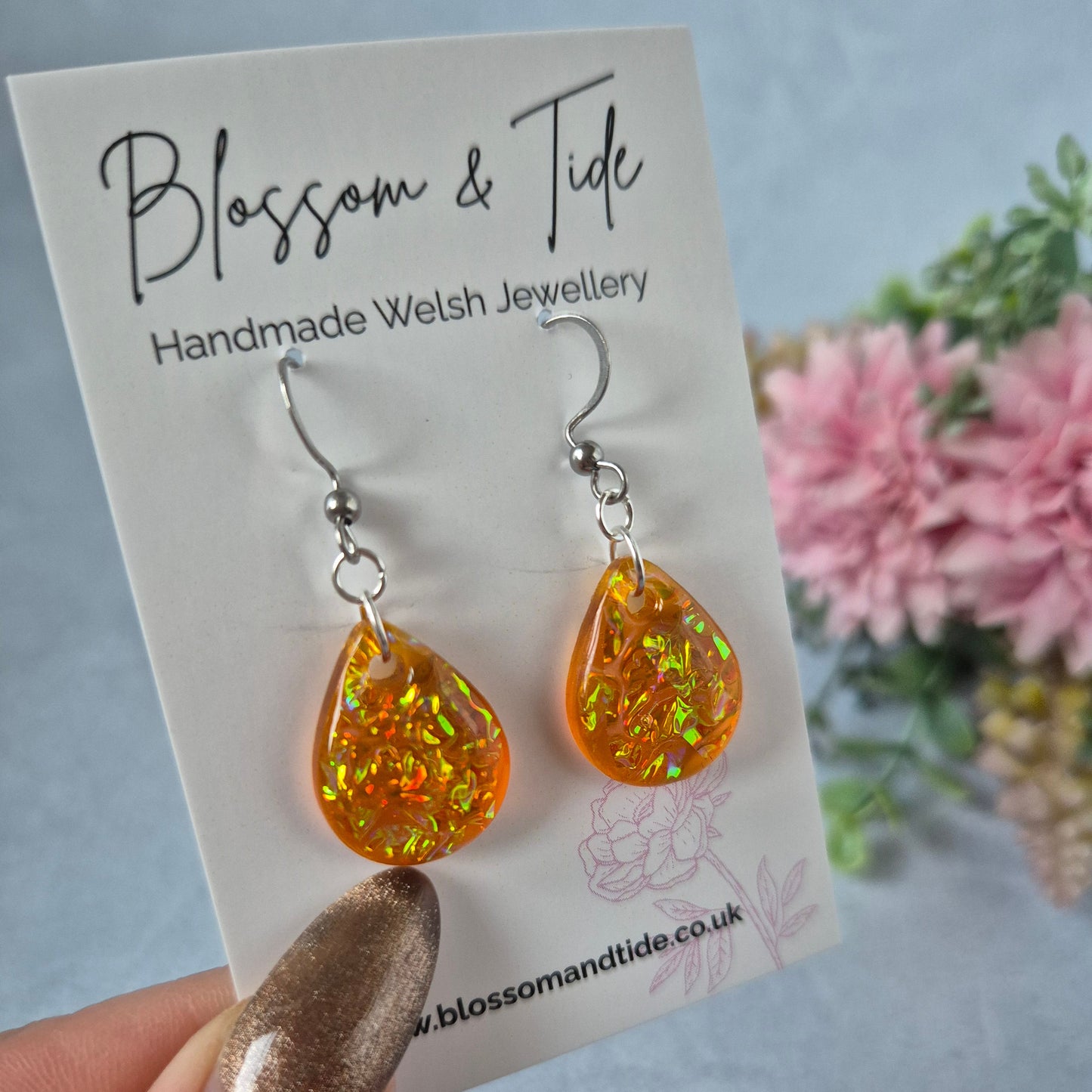 Teardrop shape orange dichroic resin earrings on branded card, against a blue background