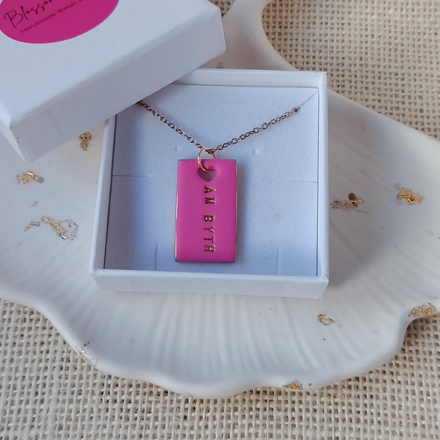 necklace with pink clay pendant in a white box on a textured surface