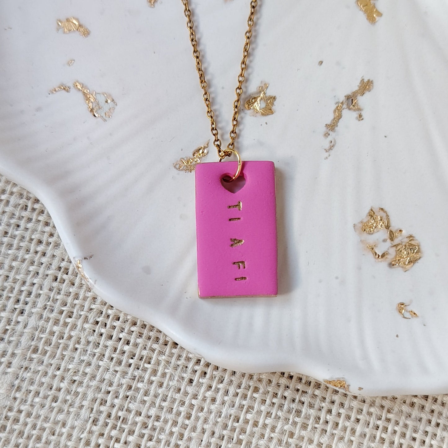 Pink polymer clay rectangular pendant with gold chain on a textured white surface