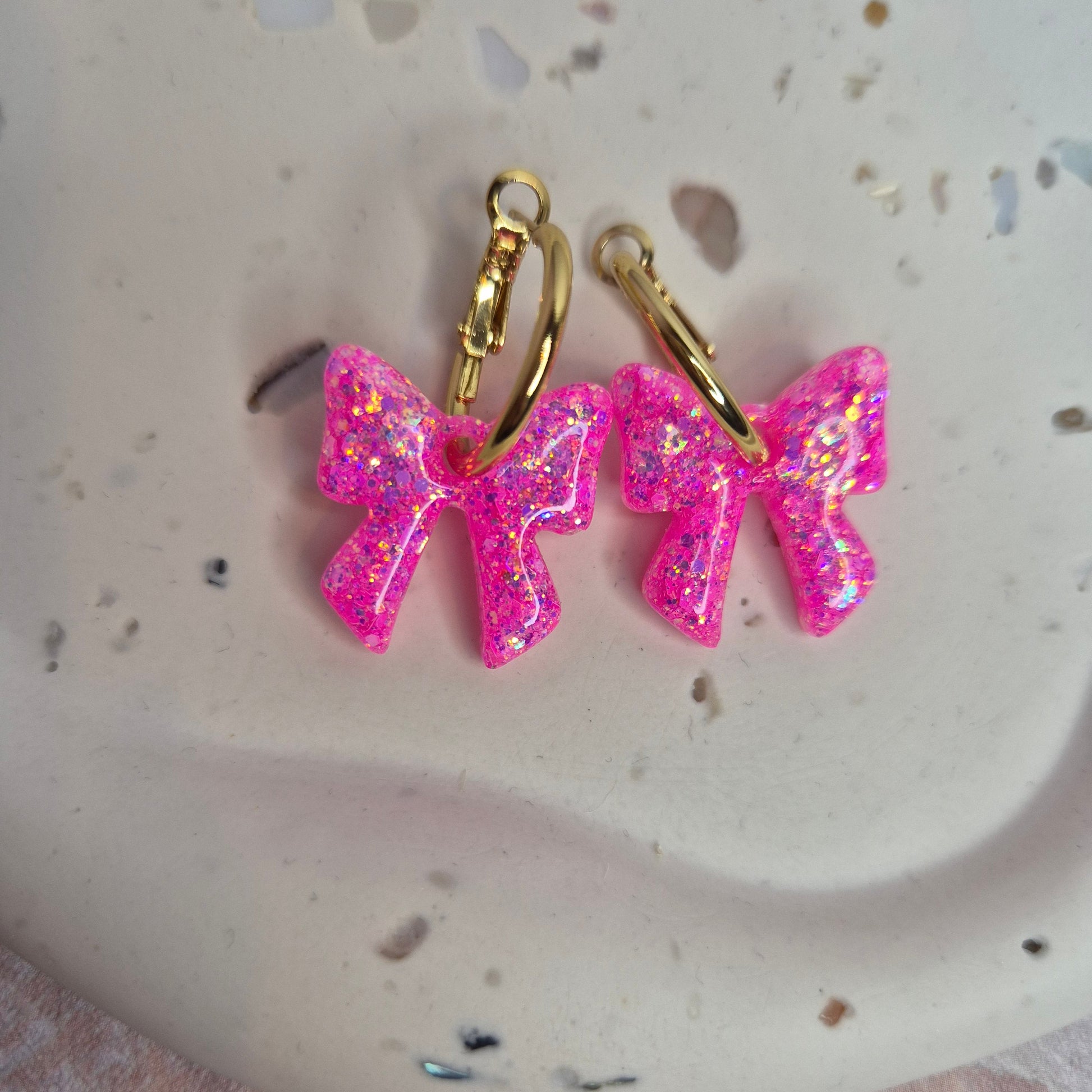 Pink glittery bow-shaped earrings on a textured white surface