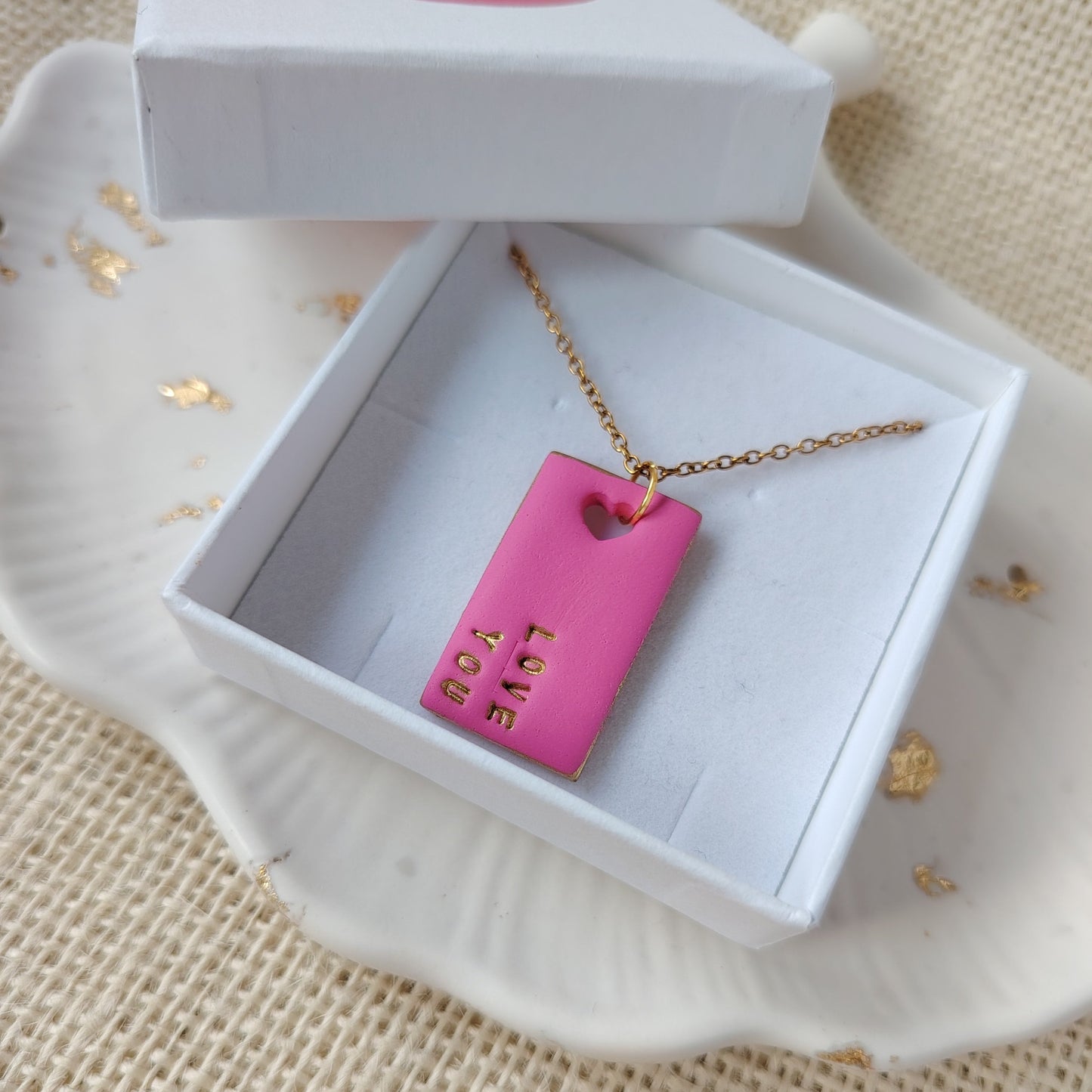 Pink necklace with gold chain in a white box on a textured beige surface