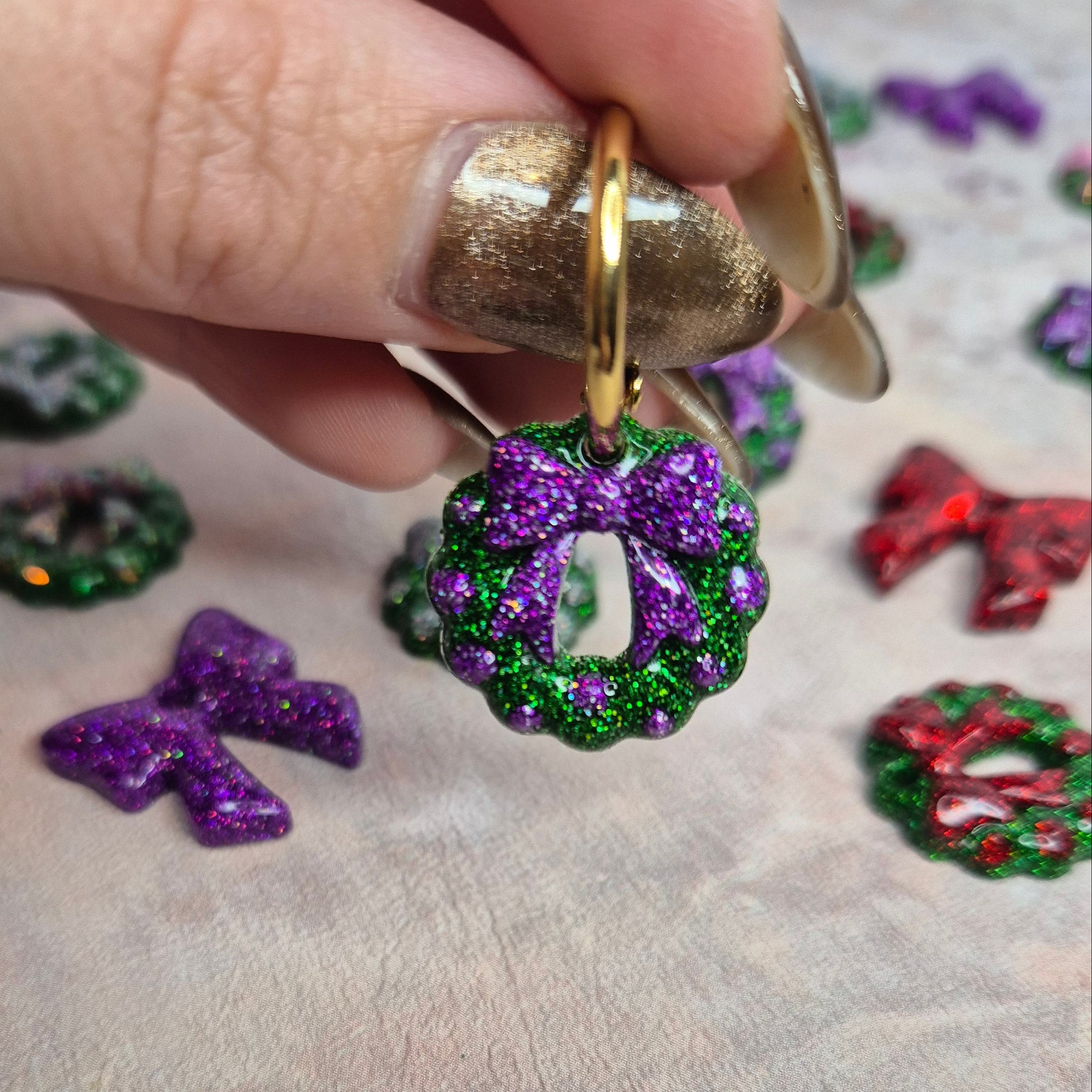 Colorful decorative wreath earrings on a textured surface with a hand holding one earring.