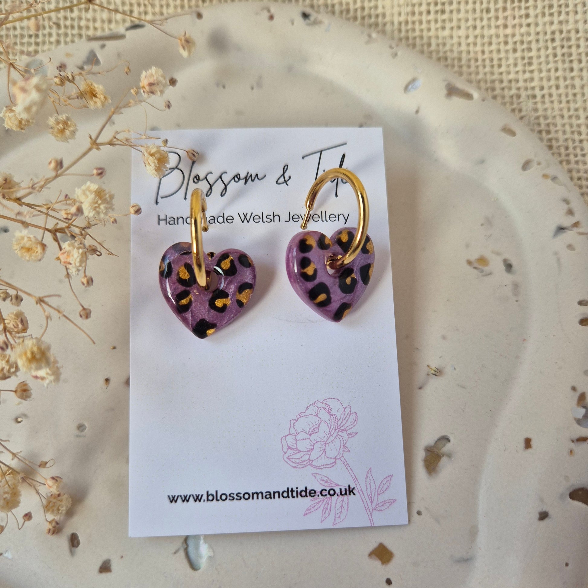 Purple and gold earrings on a branded card with a natural background
