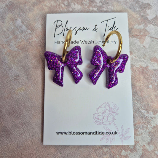 Purple glittery earrings on a card with 'Blossom & Tide' branding.