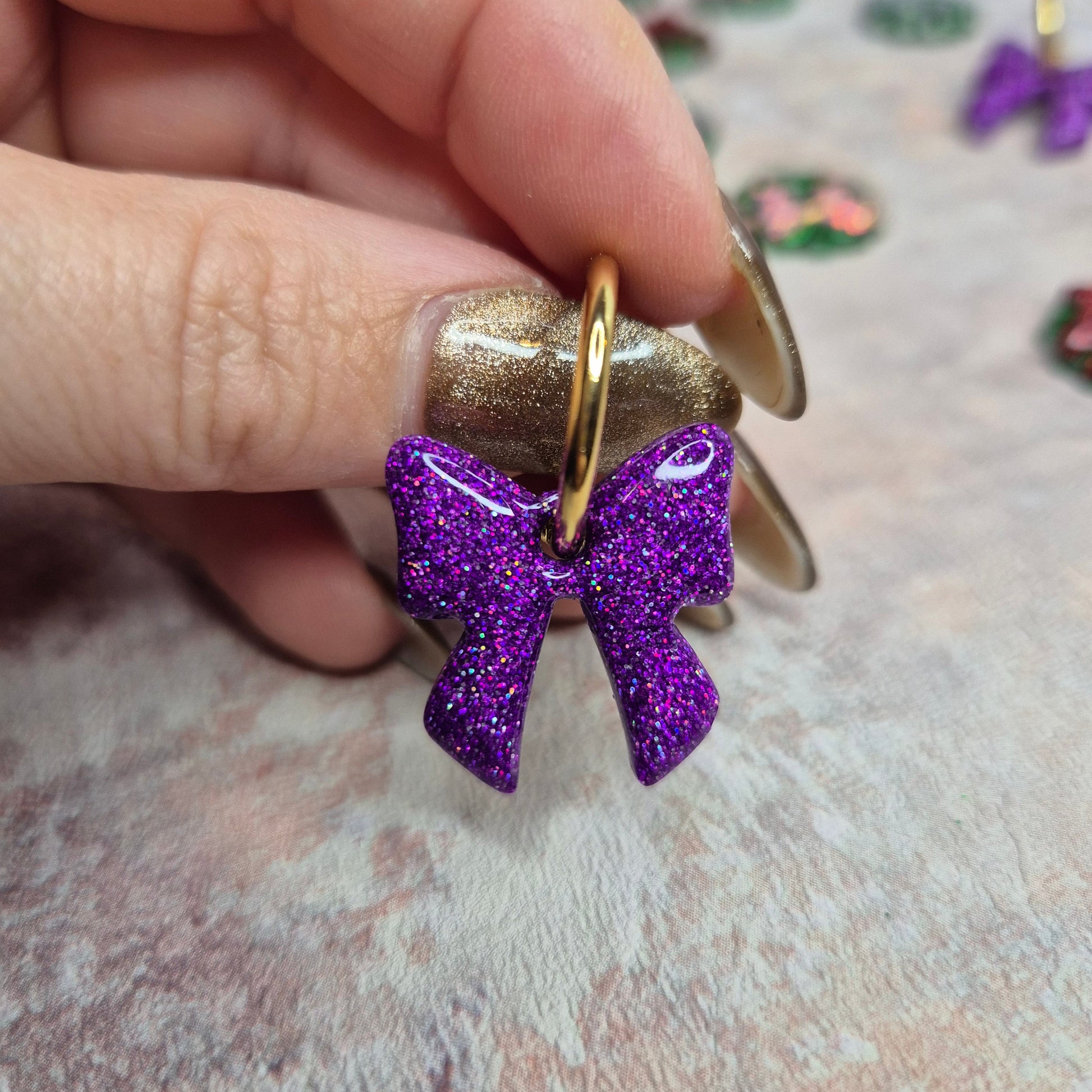 Purple glittery bow earring held by a hand against a neutral background