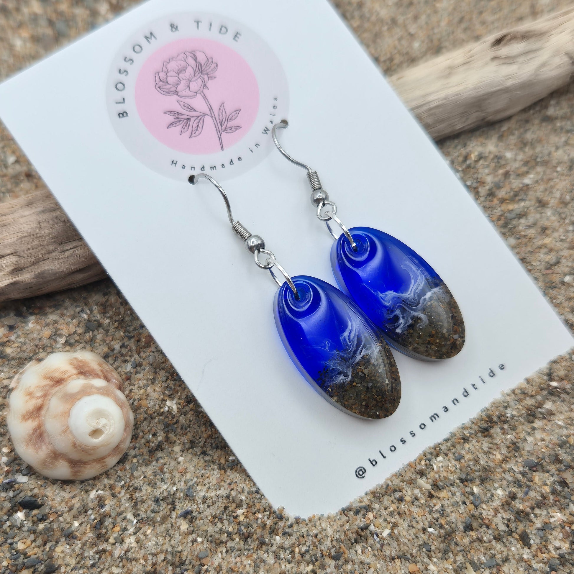 Handmade blue oval drop earrings. Made with real sand from Welsh beaches. Replicating the look of sea and sand. Displayed on a blossom and tide branded earring card.