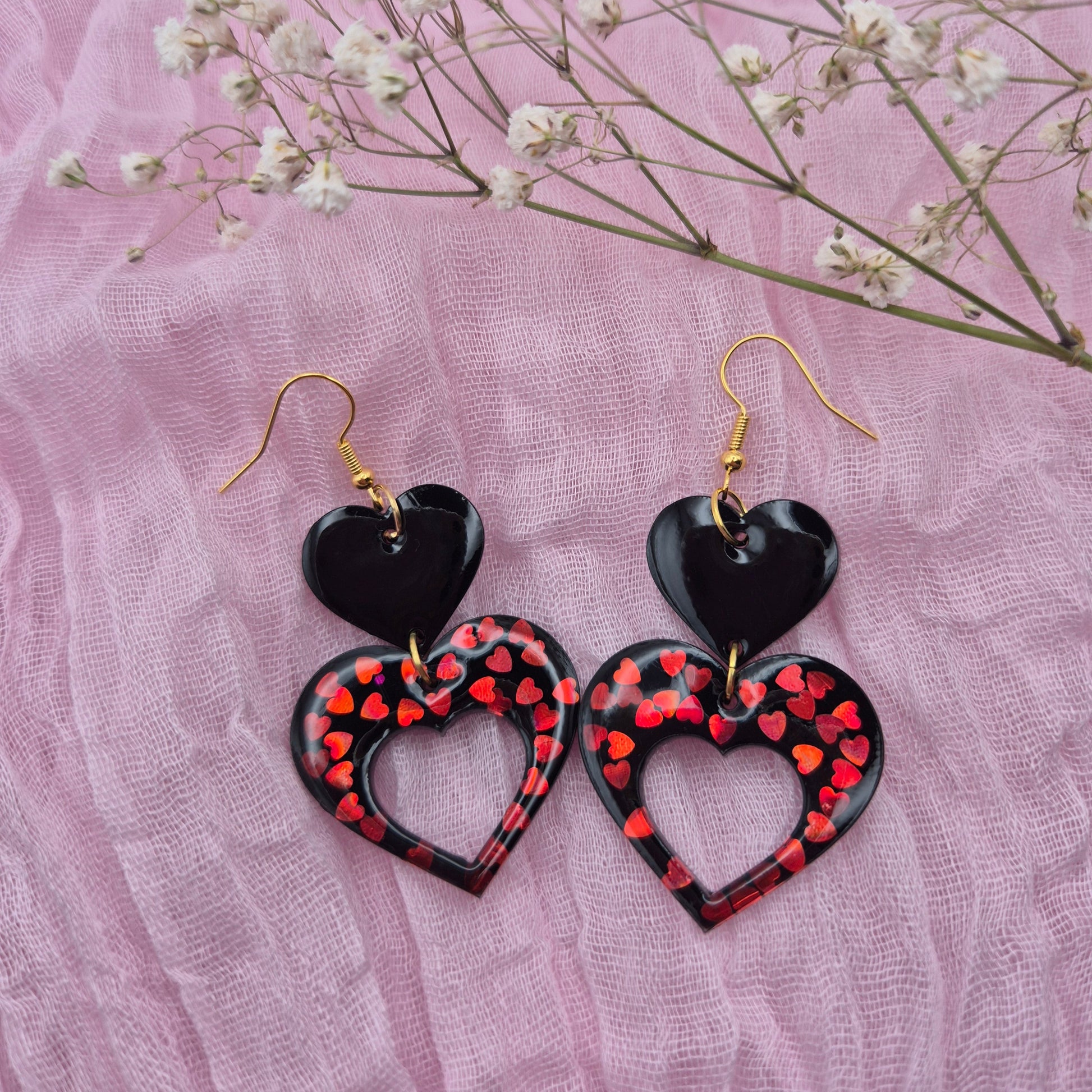 Two-tiered heart earrings with red glitter hearts and black resin.