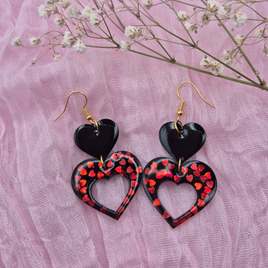 Two-tiered heart earrings with red glitter hearts and black resin.