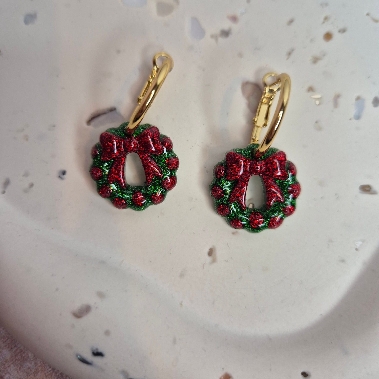 Red and green wreath earrings on a speckled surface