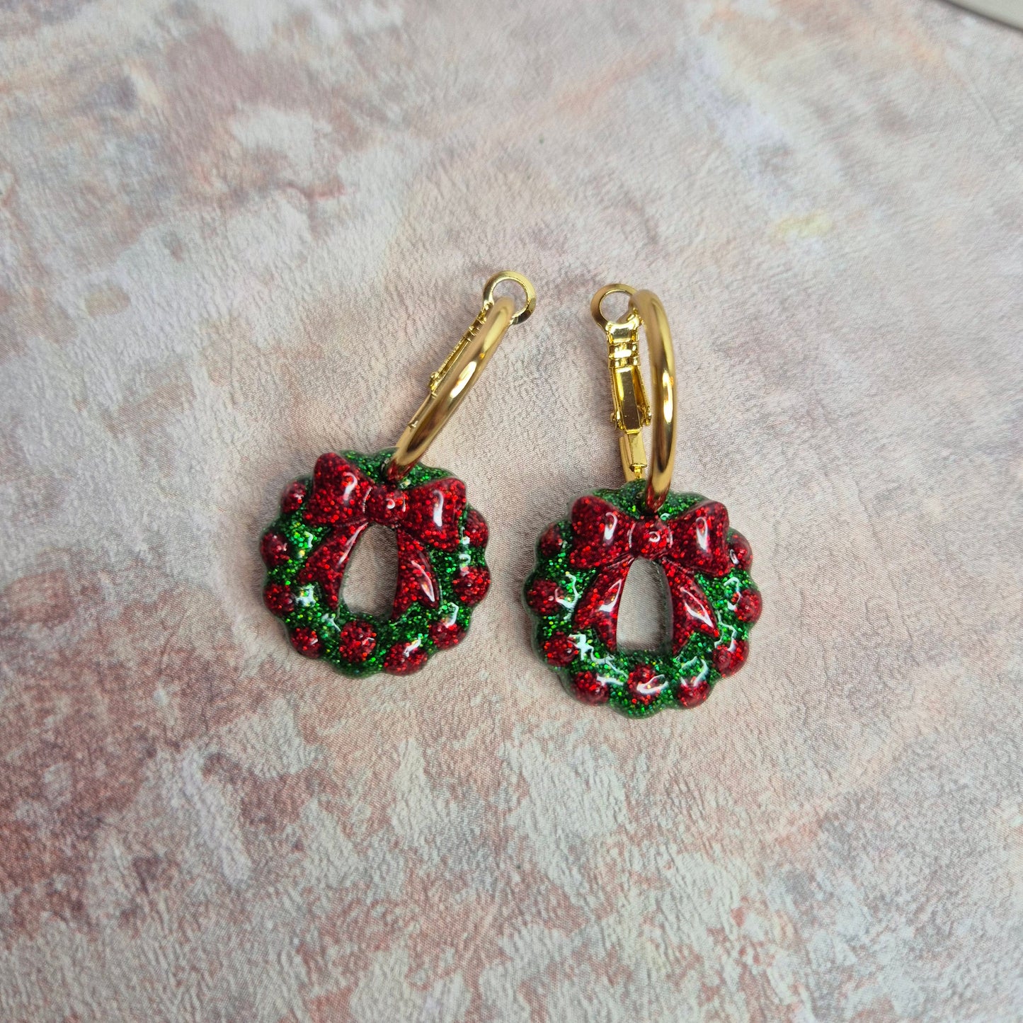 Red and green wreath-shaped earrings on a marble surface