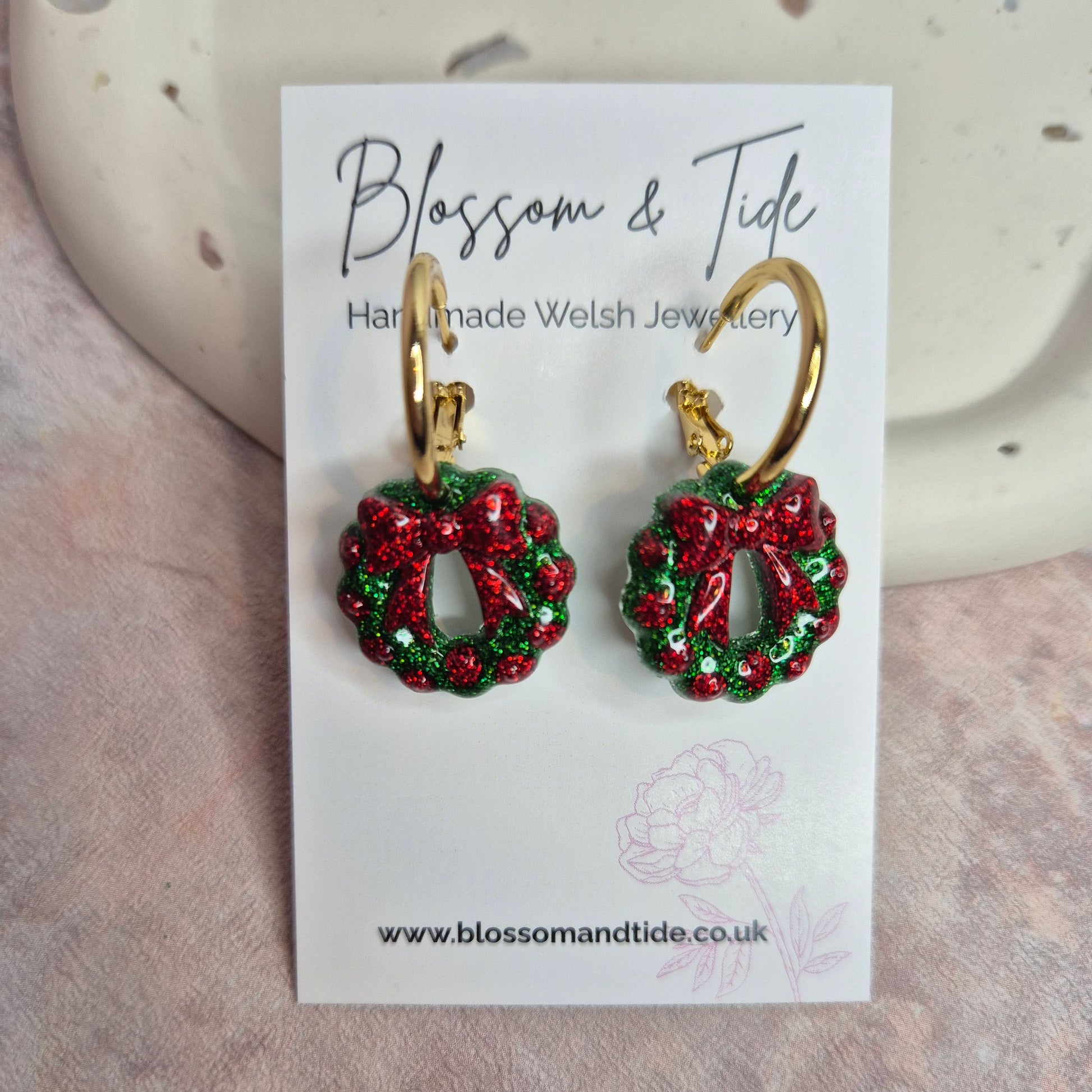 Red and green wreath earrings on a 'Blossom & Tide' card.