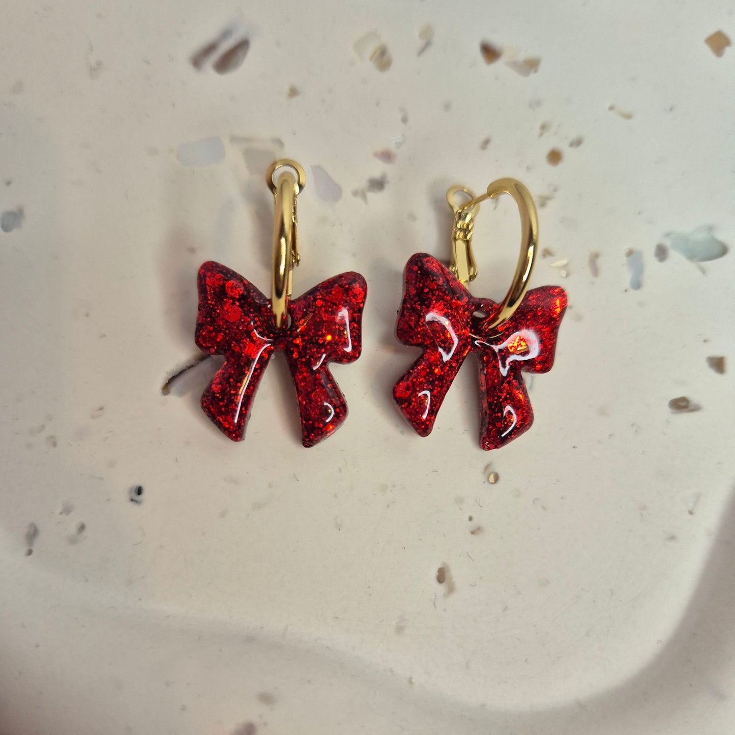 Red bow-shaped earrings on a speckled ceramic plate