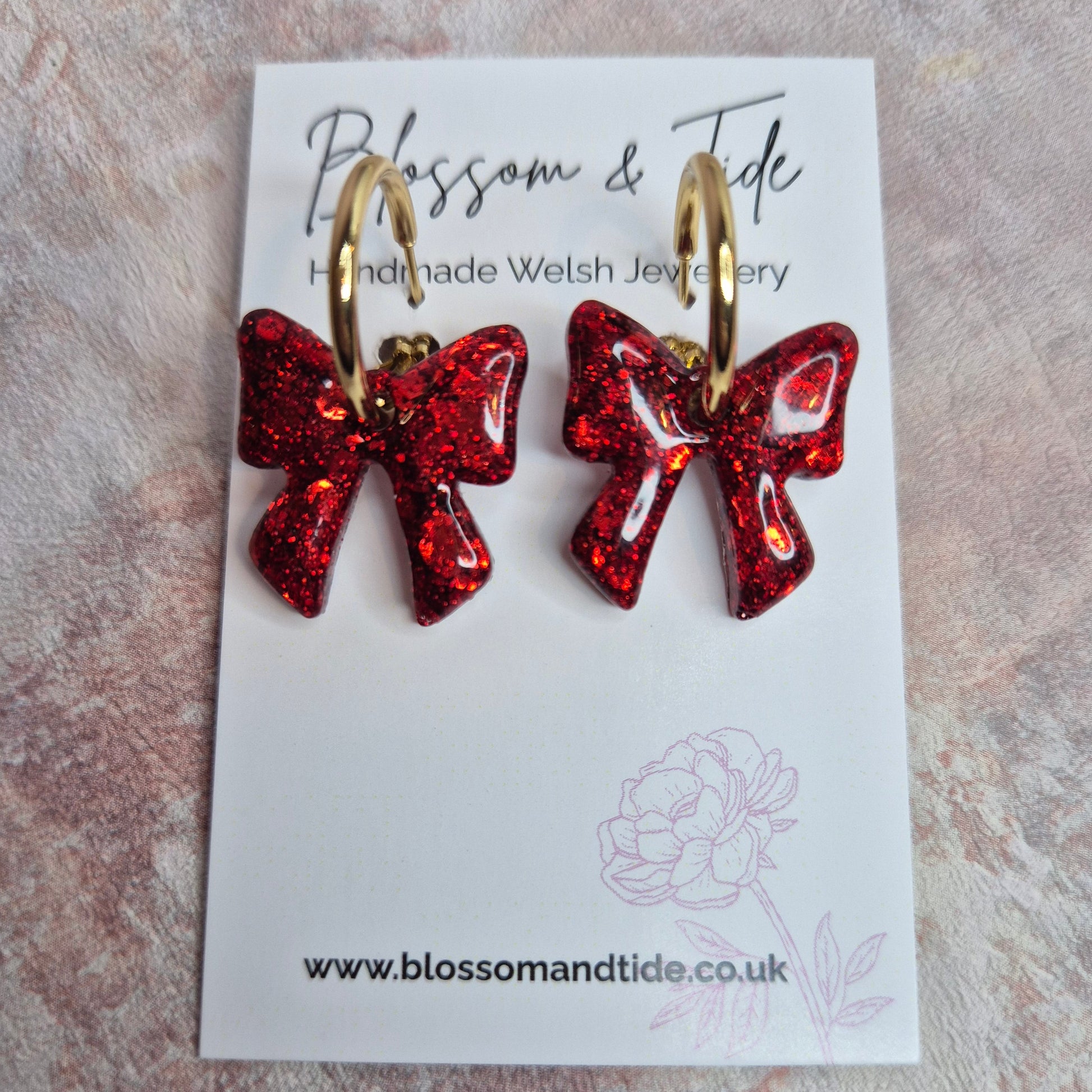 Red bow-shaped earrings on a branded card with a textured background