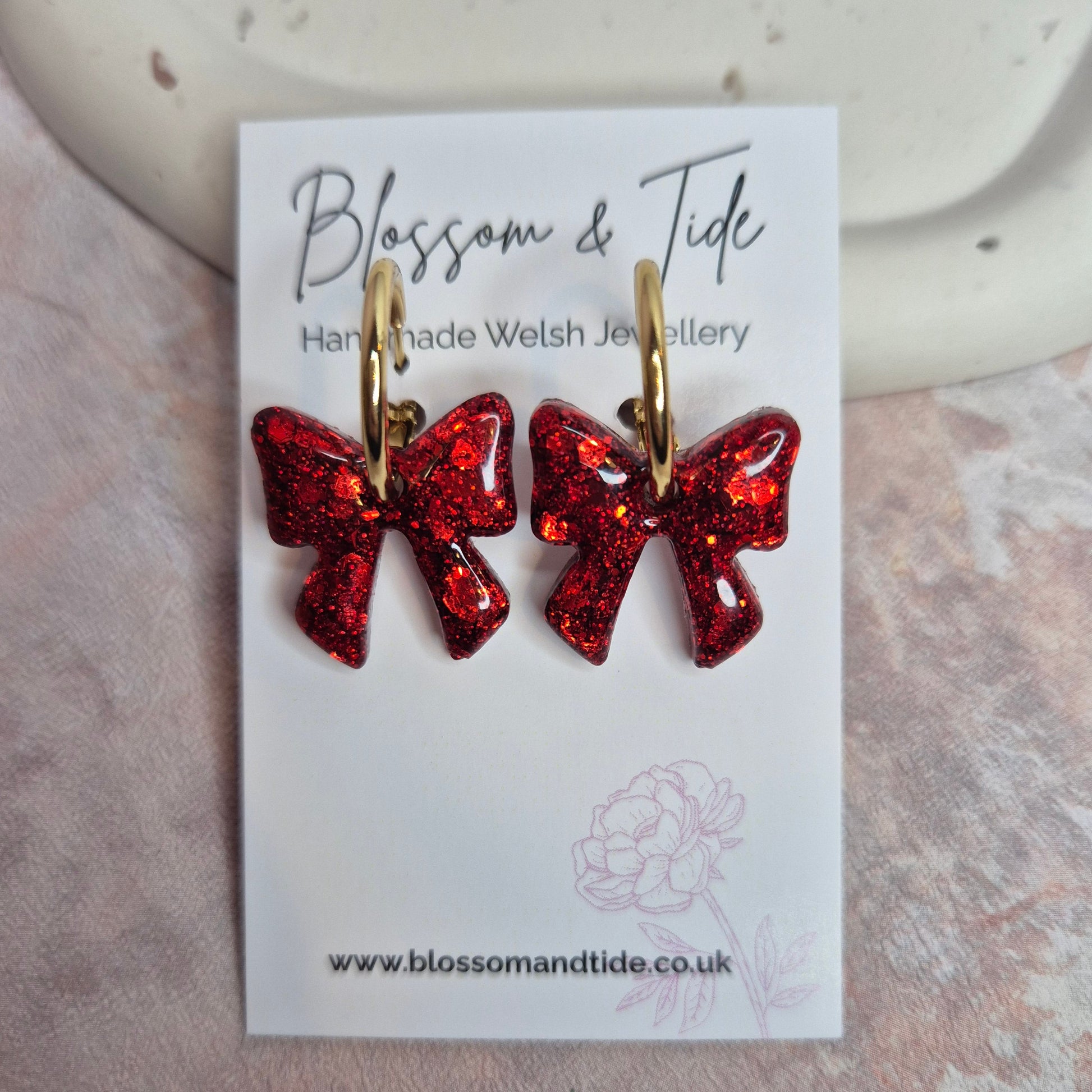 Red glittery bow-shaped earrings on a branded card with a light background