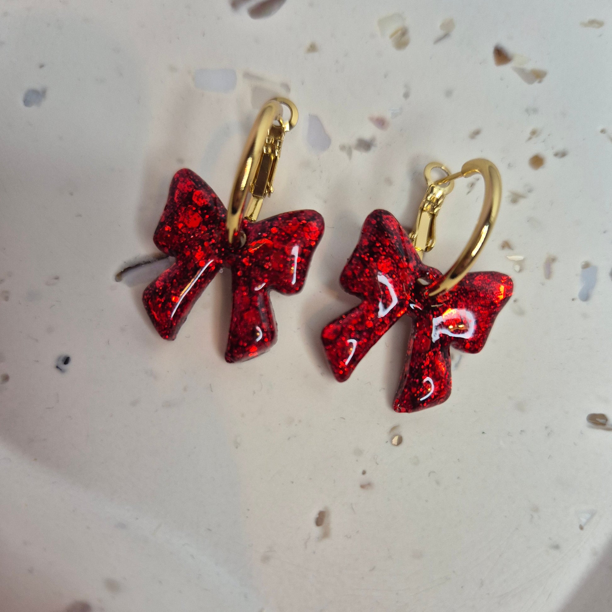 Red glittery bow-shaped earrings on a speckled surface