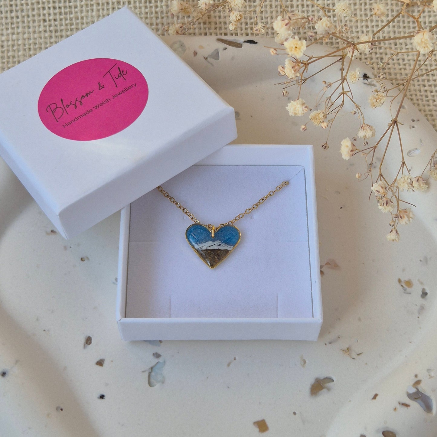 Necklace with a blue sea pendant in a white box on a textured surface