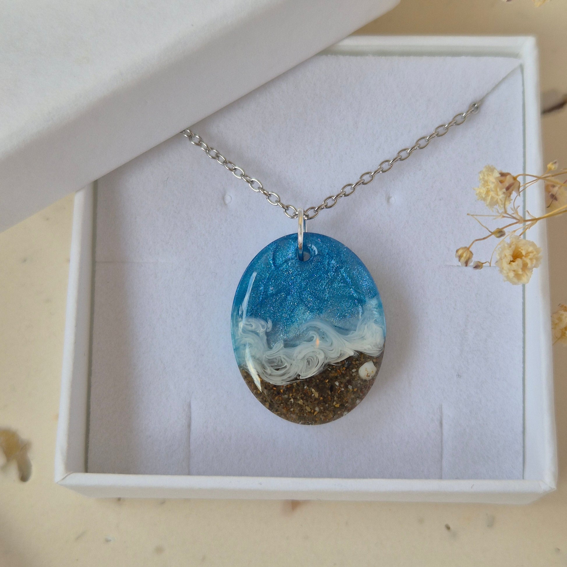 Necklace with a oval pendant featuring sand and sea design in a white box.