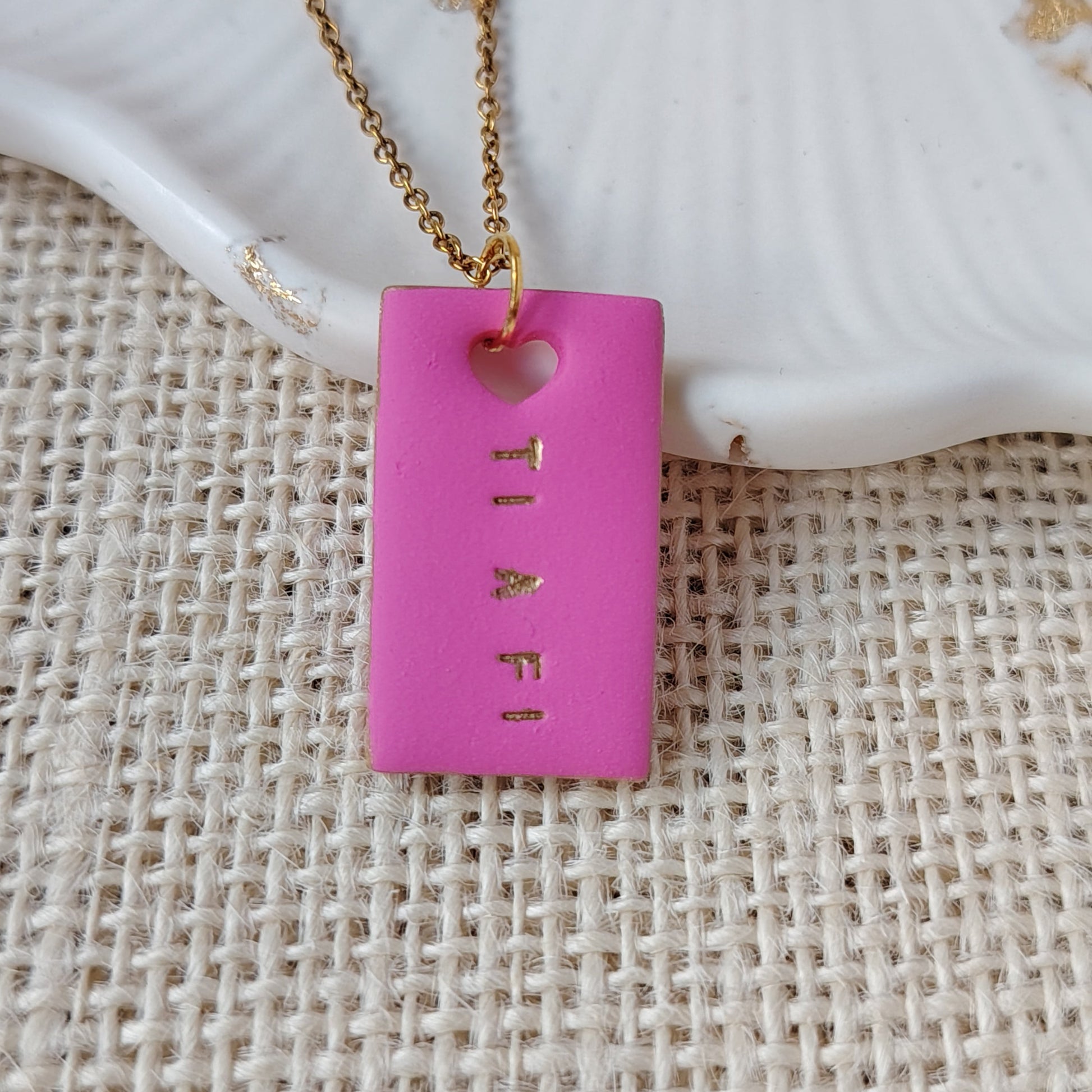 Pink rectangular pendant with gold chain on textured surface