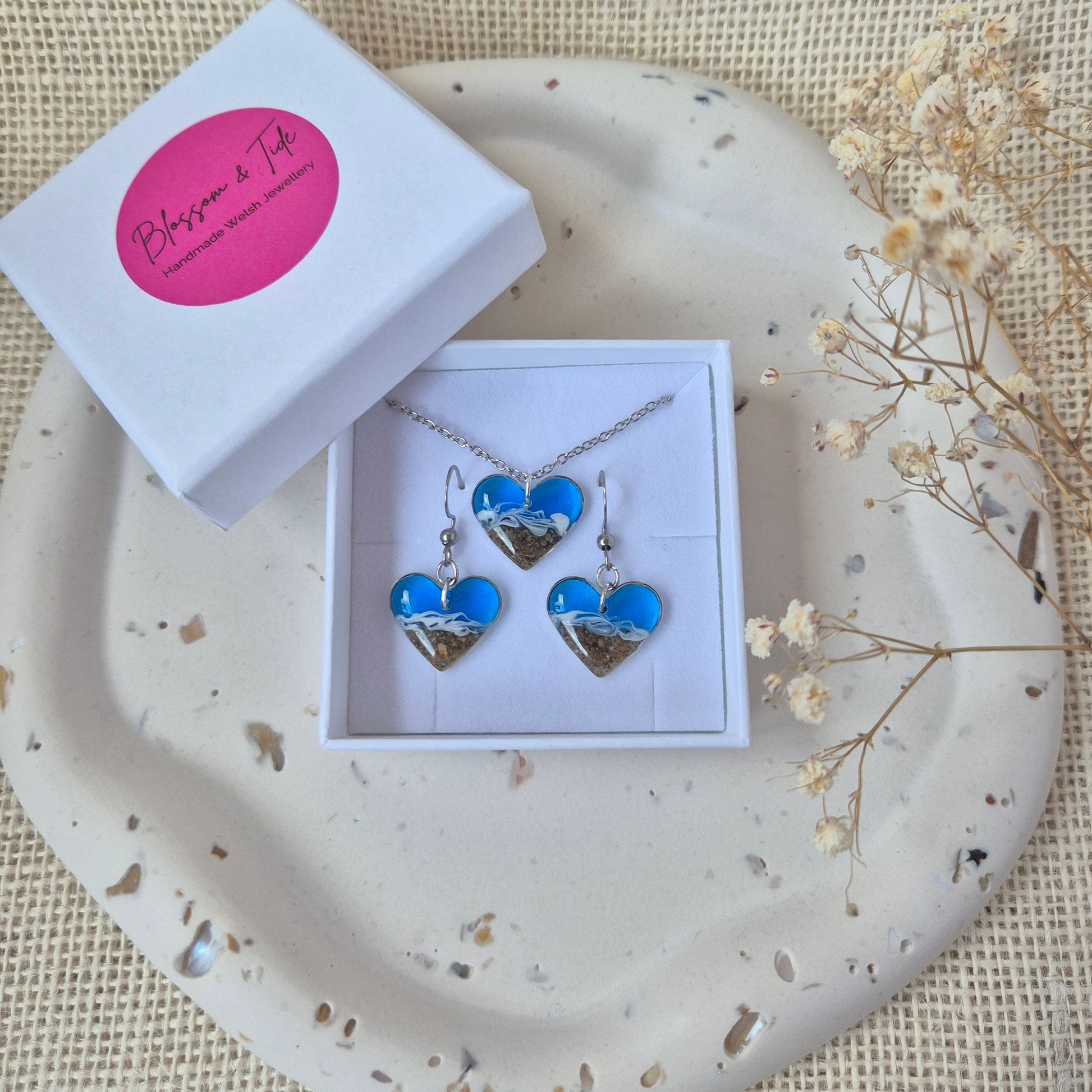 heart earrings  and necklace with beach theme in a white box on a textured surface with flowers.
