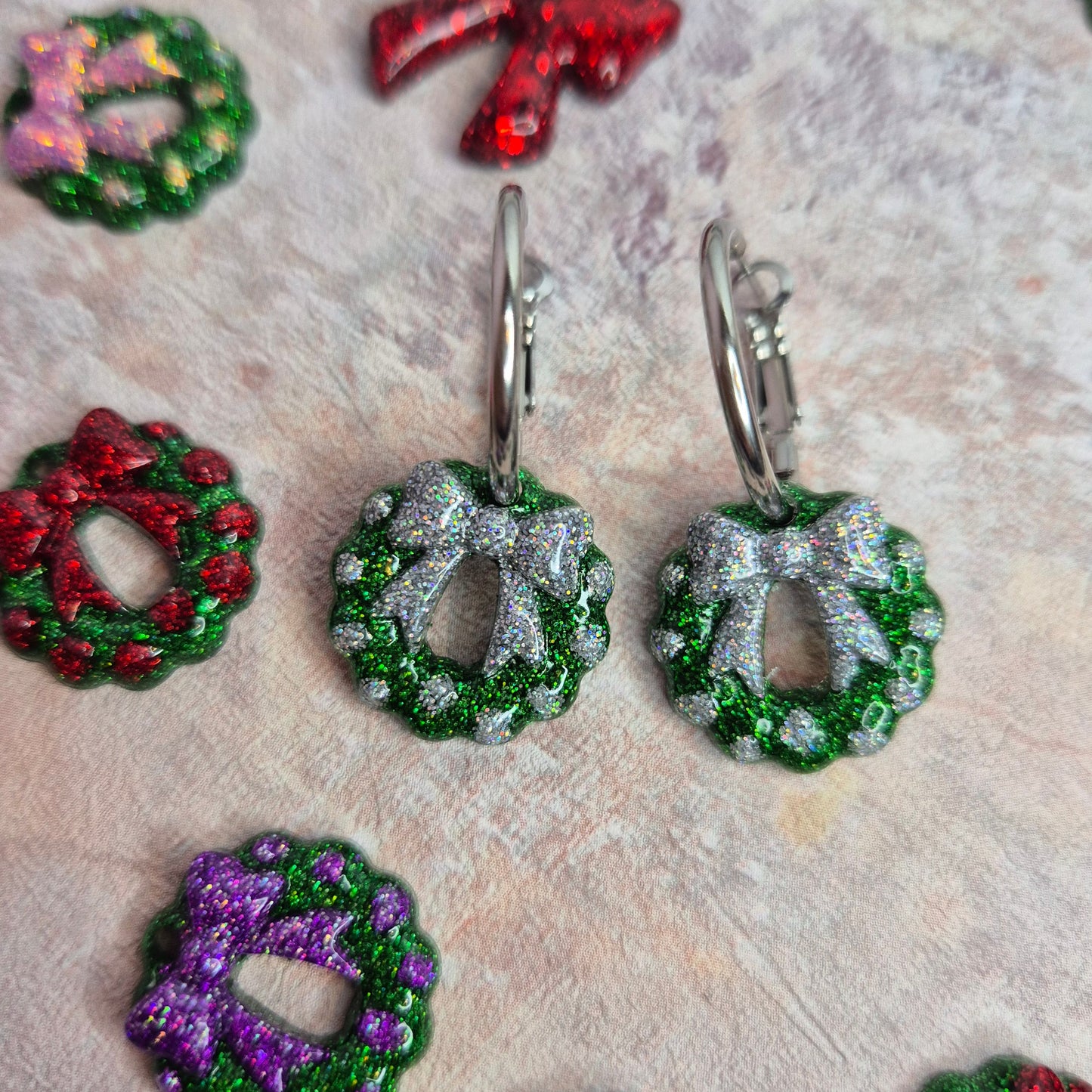 Decorative earrings shaped like wreaths and bows on a textured surface